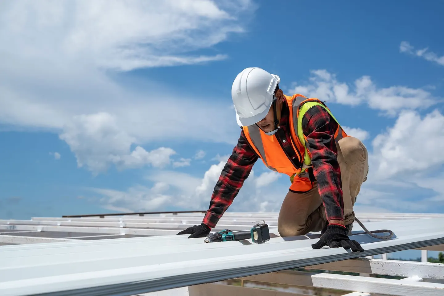 Roofer in gloves and hard hat screwing down new steel roof sheets